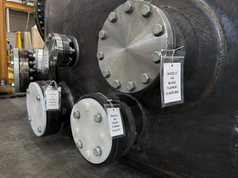 Close-up of pressure vessel nozzle flanges fitted with steel blind flanges and HDPE blanks, with individually tagged bolt bags attached for export shipping